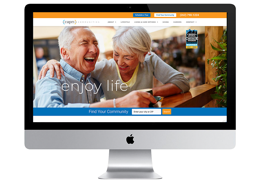 A computer screen displays a website showing a happy senior couple laughing together at a table, with the words “enjoy life” and a search bar to find communities.