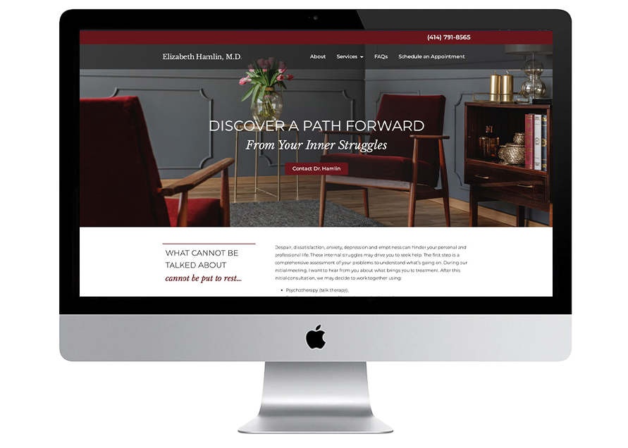 An iMac displays a psychiatrist’s website with a maroon header, a professional office photo featuring two chairs and a coffee table, and sections for about, services, FAQs, and appointment scheduling.